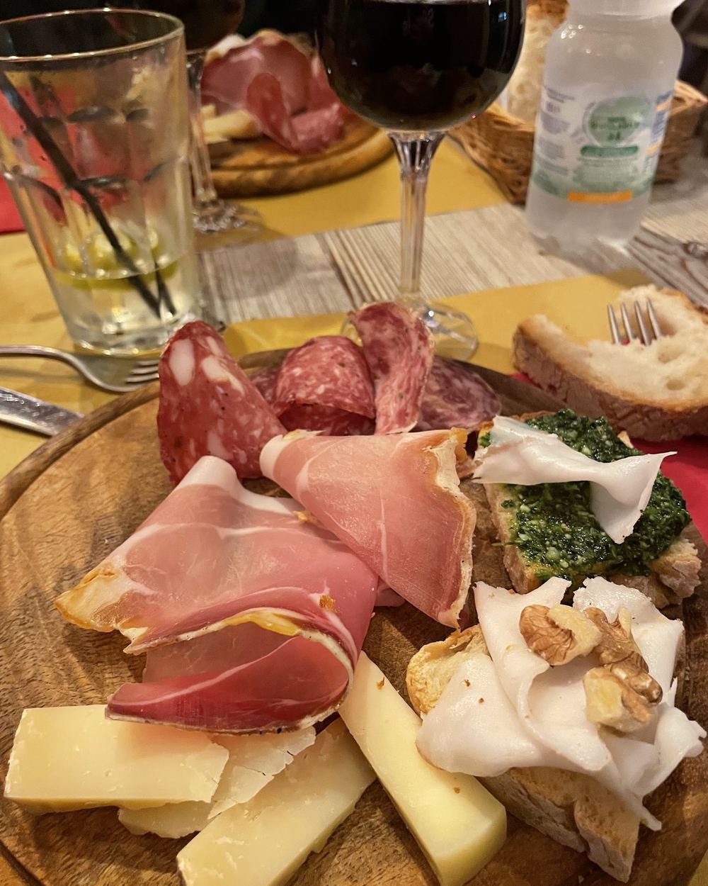 Un tagliere di legno con salumi toscani arrotolati, fette di pecorino, crostini e un calice di vino rosso accanto.